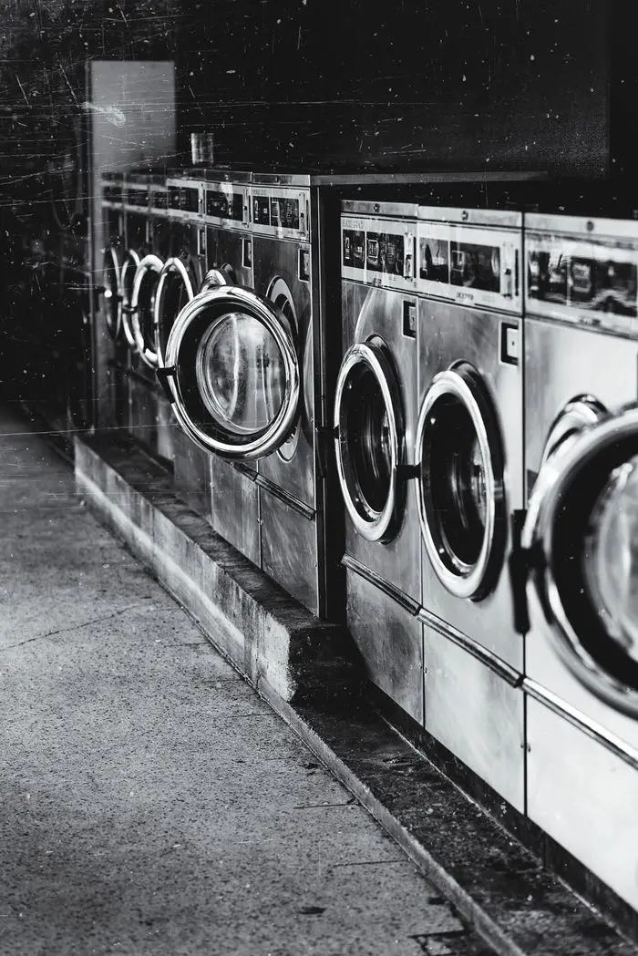 A row of industrial washing machines in an urban laundromat, showcasing steel finish.