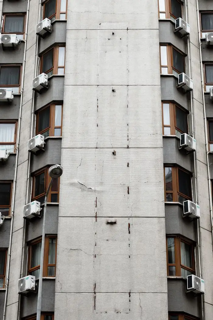 Close-up of high-rise building facade with multiple air conditioners in an urban setting.